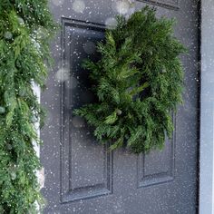 a wreath hanging on the front door of a house with snow falling all around it