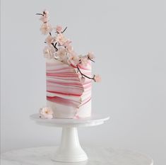 a pink and white striped cake with flowers on top is sitting on a marble pedestal