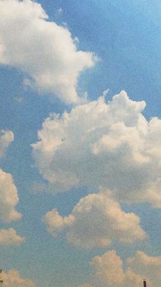 two giraffes standing in an open field under a blue sky with clouds