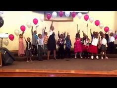 children are standing on the stage with their arms in the air and holding up balloons