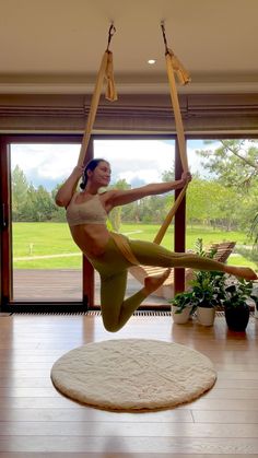 a woman is doing aerial yoga on a hammock in the middle of a living room