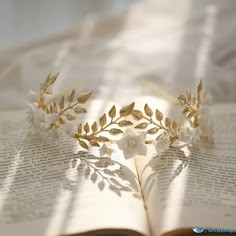 an open book with gold leaves and white flowers on top of it, sitting on a bed