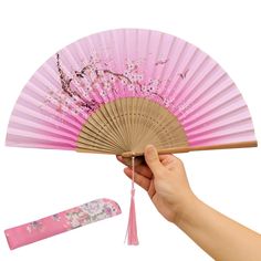 a hand holding a pink fan with cherry blossoms on it next to a pen and eraser