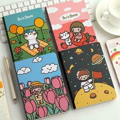 two notebooks with cartoon characters on them sitting next to a keyboard and coffee cup