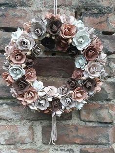 a wreath made out of paper flowers hanging on a brick wall