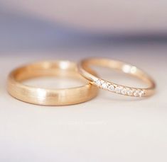 two gold wedding bands with diamonds on them sitting next to each other in front of a white background