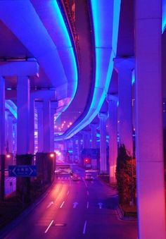 an empty highway with blue lights on the sides and cars driving down it at night