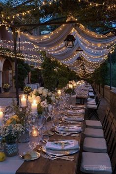 an outdoor dinner table set with candles and flowers on the table, surrounded by string lights