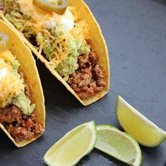 two tacos with meat, cheese and guacamole on them next to sliced limes