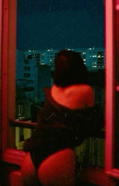 a woman sitting on a window sill looking out at the city