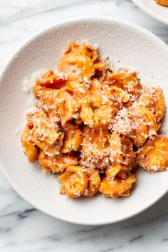 two white bowls filled with pasta covered in sauce and parmesan cheese on top