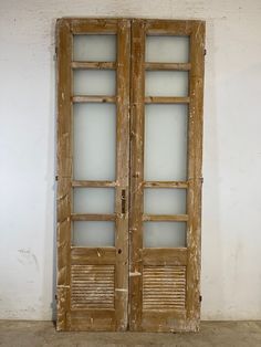 an old wooden double door with glass inserts on the sides and side panels, in front of a white wall