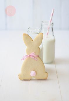 a cookie shaped like a bunny sitting next to a jar of milk and a straw