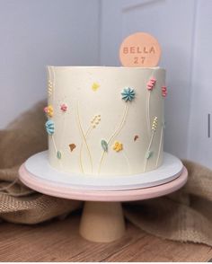 there is a white cake with flowers on the side and a name plate that says bella 27