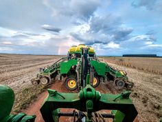 two large green tractors are in the middle of a field