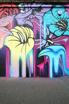 a wall painted with colorful graffiti and flowers on it's side in front of a building