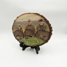 three men are sitting in the grass with their turkeys on a wooden plaque stand