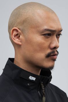 a man with a bald head and moustache looks off to the side while wearing a black jacket