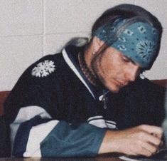 a man sitting at a table with his head in his hands and writing on a piece of paper