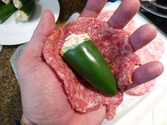 a person holding a piece of meat with a green pepper on it and some other food in the background