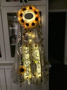 a sunflower clock hanging from the side of a door with ribbons and lights around it