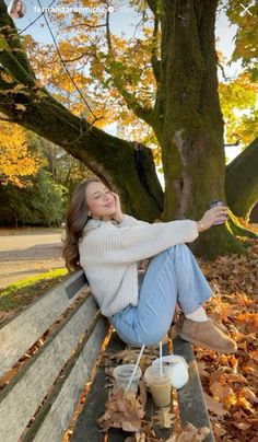 a woman sitting on top of a wooden bench next to a cup of coffee and a tree