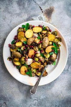 a white plate topped with potatoes and pomegranates next to a fork