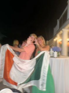 two people holding an irish and american flag in front of a building at night time