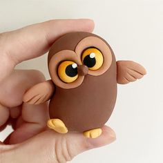 a hand holding a small brown toy with yellow eyes and an owl on it's back