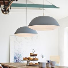 a wooden table topped with plates of food under two lamps hanging from the ceiling above it