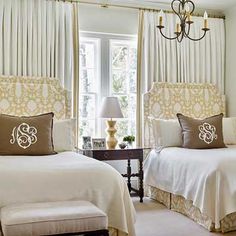 two twin beds in a bedroom with white walls and drapes on the windowsill