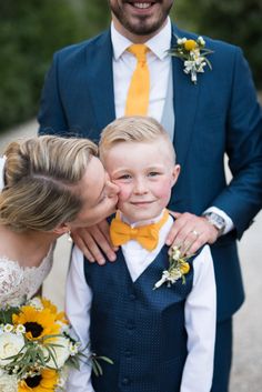 a man in a blue suit and yellow tie kissing a little boy with his mother