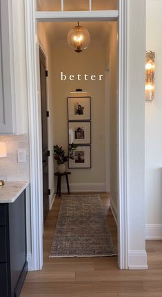 an entry way leading to a kitchen and living room with white walls, wood flooring and framed pictures on the wall