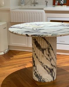 a marble table in the middle of a kitchen with white cabinets and wood flooring