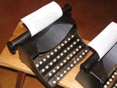 two old typewriters with paper on them sitting on a wooden table next to each other