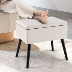 a woman laying on top of a white ottoman with her feet resting on the foot rest