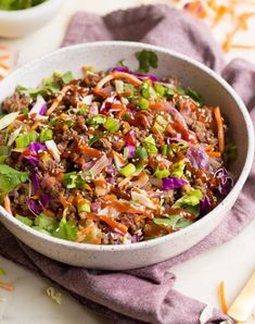 a white bowl filled with salad on top of a purple cloth next to two bowls