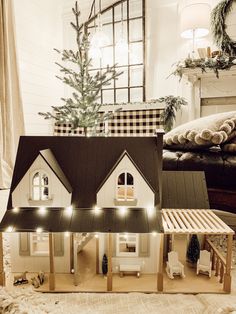 a doll house with lights on in front of a christmas tree