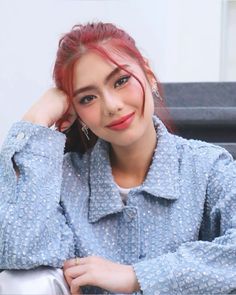 a woman with red hair and blue shirt posing for a photo in front of stairs