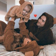 a man and woman laying on top of a bed with a baby in a bear costume