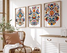 three framed pictures hang on the wall above a wicker chair in a white room