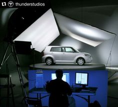 a white minivan is on display in front of a blue backdrop with a man standing next to it