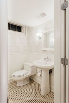 a white toilet sitting next to a sink in a bathroom on top of a black and white checkered floor