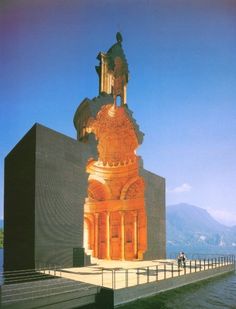 a tall building with a statue on top of it's side next to the water