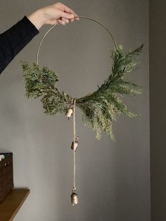 a person holding a wreath with bells and greenery hanging from it's side