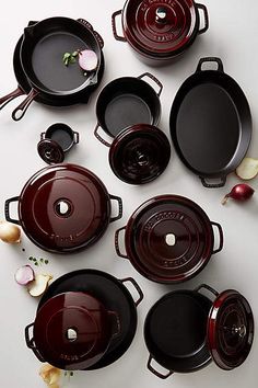 many pots and pans are arranged on a white surface with onions in the foreground