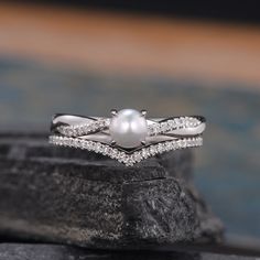 a white pearl and diamond ring sitting on top of a rock