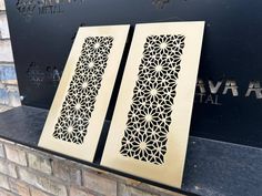 two laser cut panels sitting on top of a brick wall next to a black sign