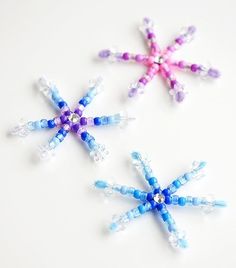 three snowflakes made out of beads on a white surface with blue, pink and purple colors