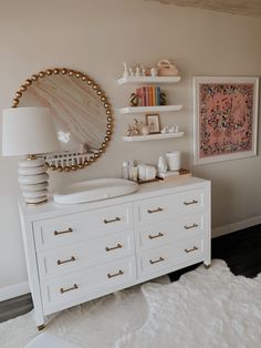 a white dresser sitting next to a wall with shelves on it and a mirror above it